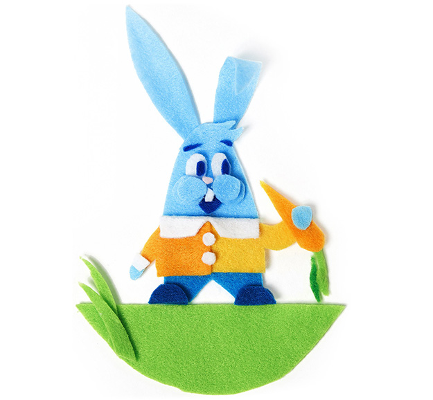 blue rabbit with orange sweater holding a carrot standing on grass