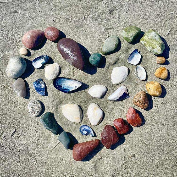 Colorful seashells and rocks creatively positioned in the sand on the beach, forming a heart