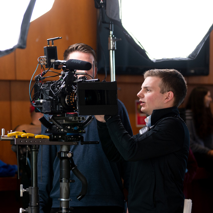 Evan working on set of a video shoot, looking at a camera