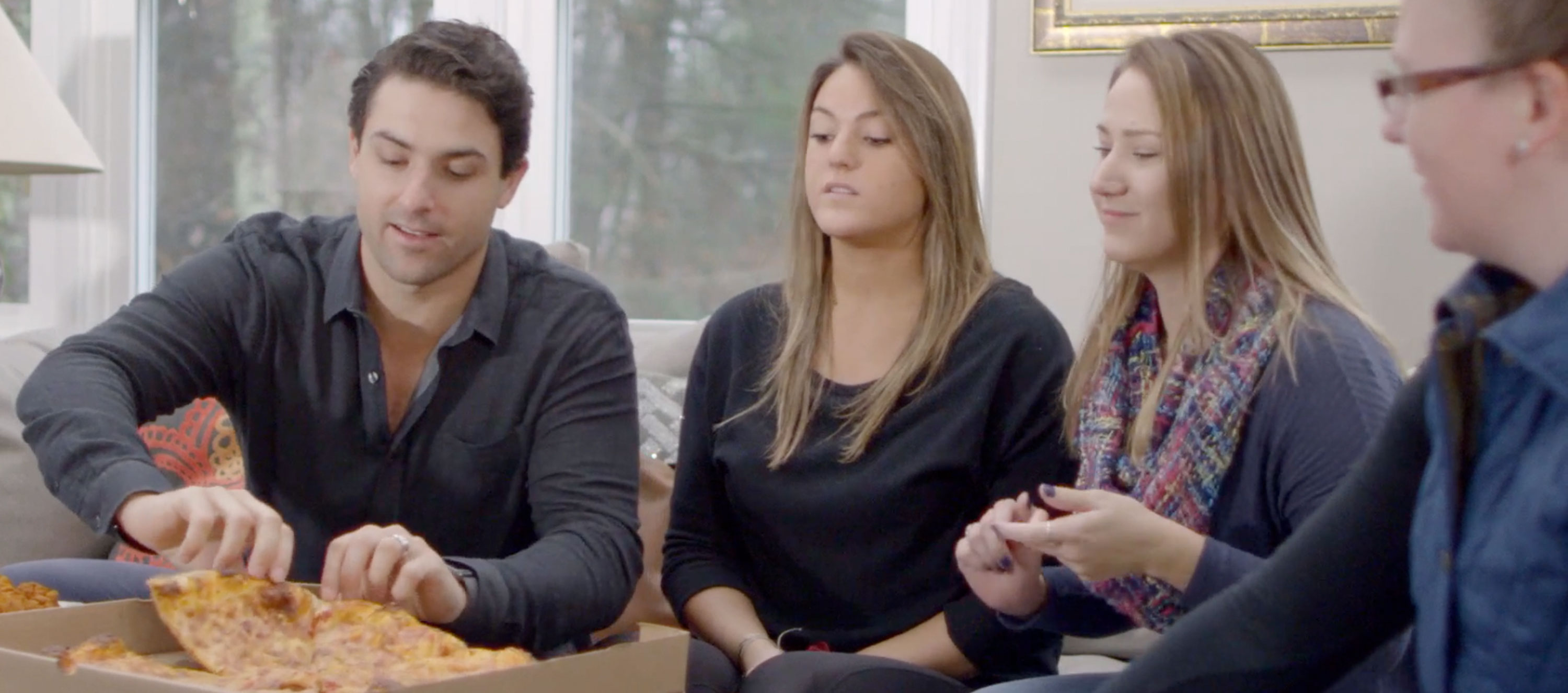 four people sitting on the couch eating pizza