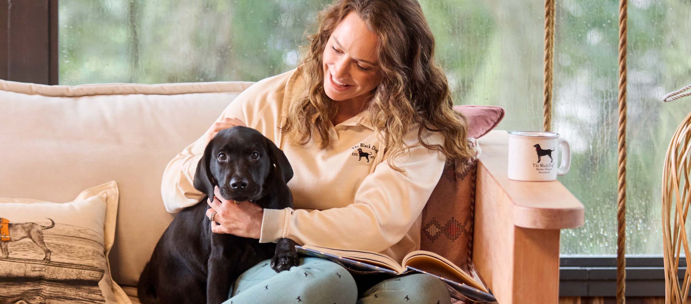 Woman sitting on couch in Black Dog apparel with a black puppy