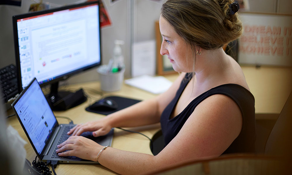 V2 Communications person working on laptop at desk