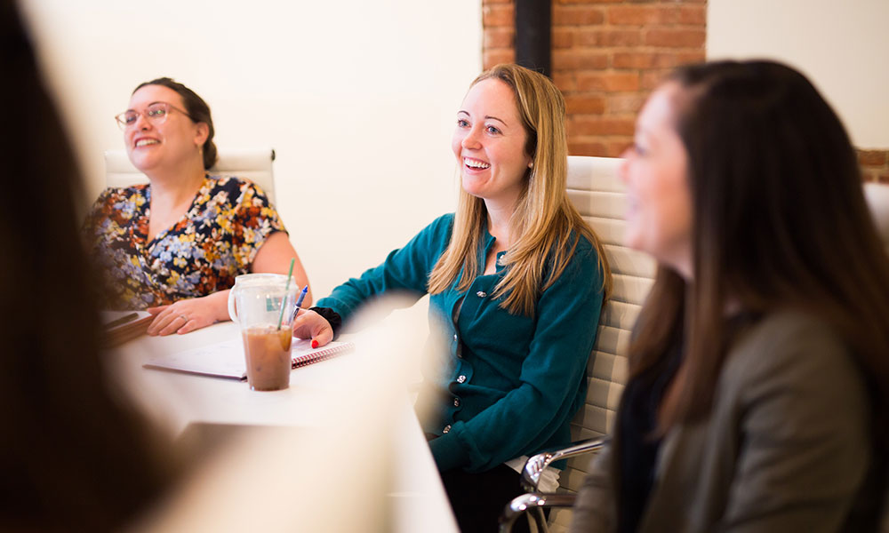 V2 Communications meeting in conference room with three people sitting around table