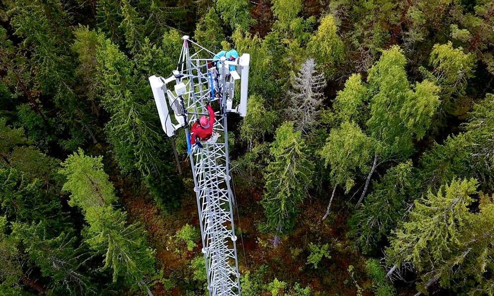 aerial view of workers on a cell tower with trees in background
