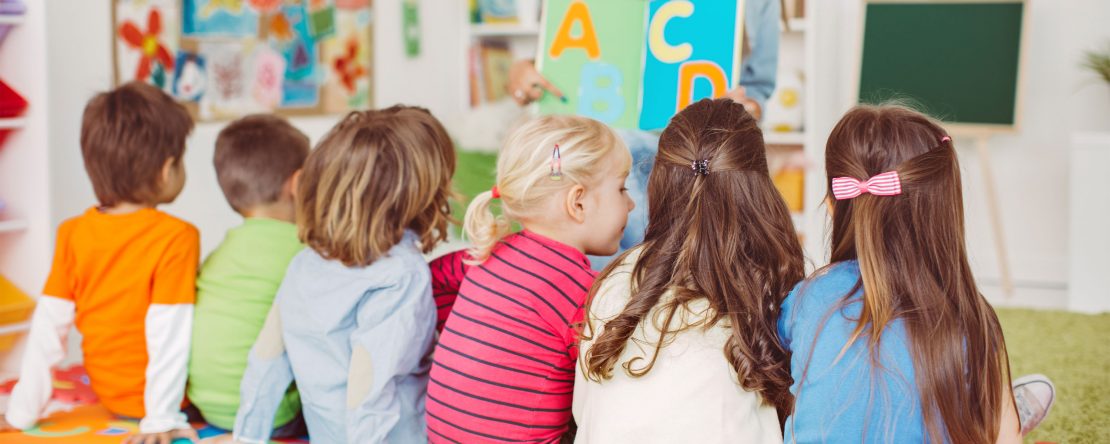 Children sitting in a classroom while a teacher reads them a book